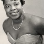 A young African American Woman in a sleeveless dress and pearls