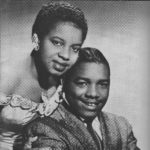 An African American couple posed in a studio photograph in semi-formal attire